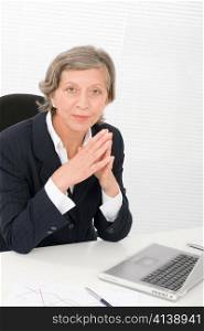 Successful senior businesswoman sitting behind office table with laptop portrait