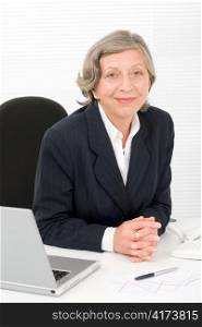 Successful senior businesswoman sitting behind office table with laptop portrait