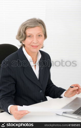 Successful senior businesswoman sitting behind office table with laptop portrait