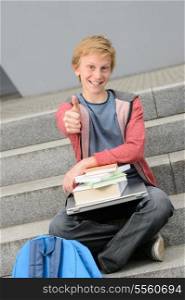 Successful student thumb-up sitting with books and laptop on steps