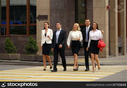 Successful Team of five business people confidently striding along the summer street