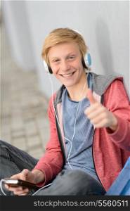 Successful teenage student thumb-up listening to music sitting outside
