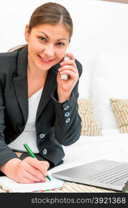 successful woman in a suit talking on the phone and making notes in a notebook