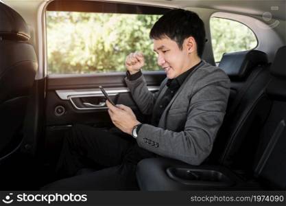 successful young business man using a smartphone while sitting in the back seat of car