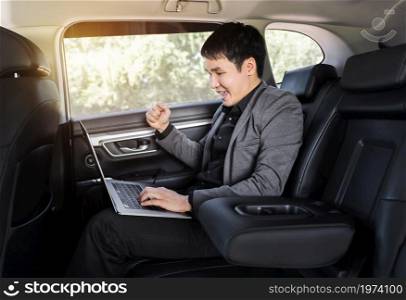 successful young business man using laptop computer while sitting in the back seat of car