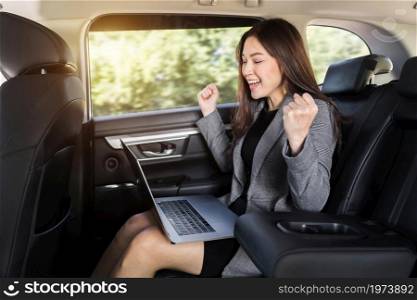 successful young business woman using laptop computer while sitting in the back seat of car