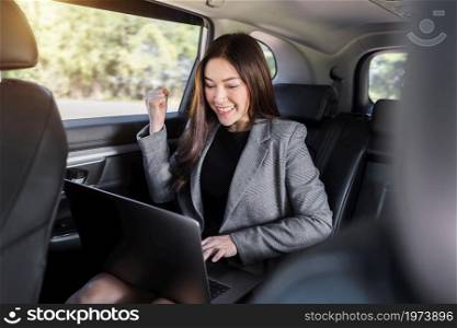 successful young business woman using laptop computer while sitting in the back seat of car