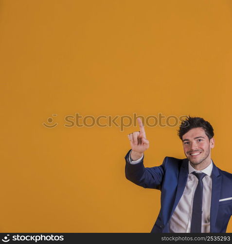 successful young businessman pointing his finger upward against orange backdrop