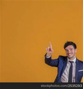 successful young businessman pointing his finger upward against orange backdrop