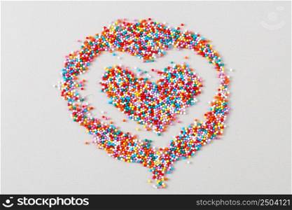 sugar baking colorful sprinkles in shape of heart on a light beige background.. sugar baking colorful pastry topping in shape of heart on light beige background.