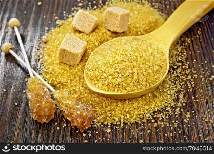 Sugar brown granulated in a spoon, cubes and crystal on a stick against a dark wooden board