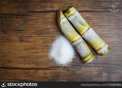 Sugar cane and white sugar on rustic wood background top view