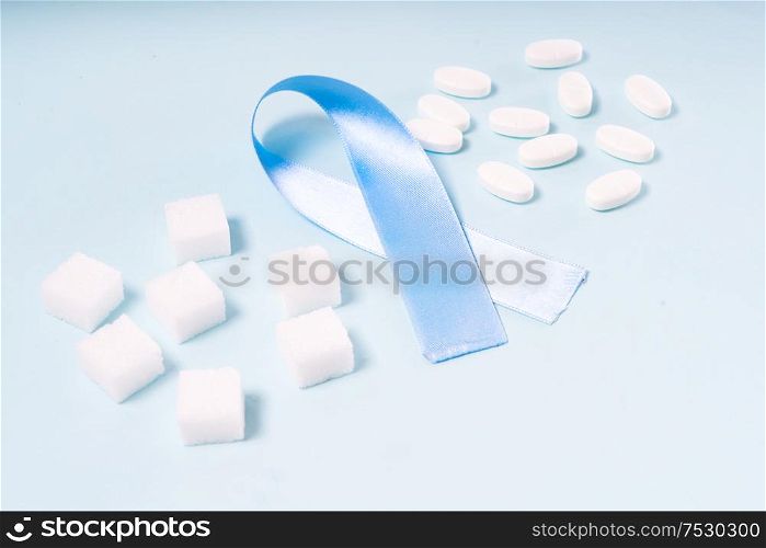 Sugar cubes, Diabetes Awareness Blue Ribbon and pills on plain blue background. World Diabetes Day concept.. Sugar on blue background