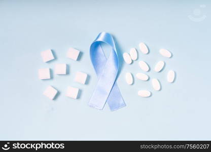 Sugar cubes, Diabetes Awareness Blue Ribbon and pills on plain blue background, flat lay scene. World Diabetes Day concept.. Sugar on blue background