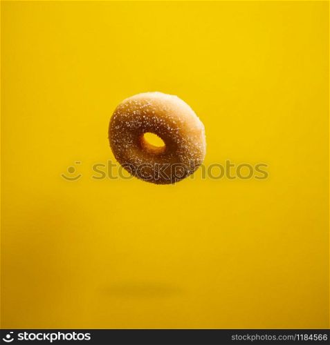 Sugar doughnut in motion falling on yelloy background. Sweet and colourful doughnuts falling or flying in motion.