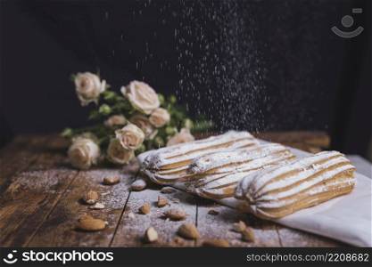 sugar powder dusted baked eclairs with almonds wooden backdrop