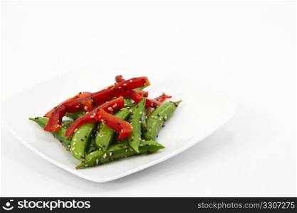 Sugar snap peas salad with garnishes of red pepper slices, black and white sesame seeds, and oil dressing on white plate; white background; copy space;