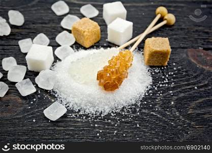 Sugar white and brown granulated, crystalline and cubes on the background of a black wooden board
