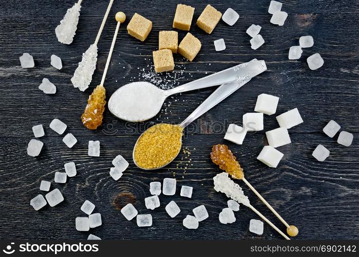 Sugar white and brown granulated in spoons, crystal and cubes on the background of a black wooden board from above