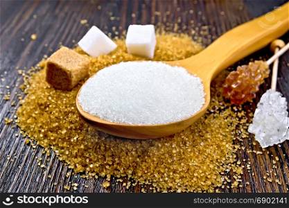 Sugar white and brown in cubes, crystal on a stick and granulated in a spoon on a wooden plank background