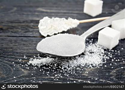 Sugar white granulated in a metal spoon, crystal and cubes on a black wooden board background