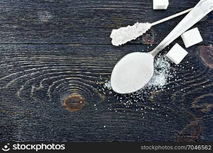 Sugar white granulated in a spoon, crystal and cubes on the background of a black wooden board from above