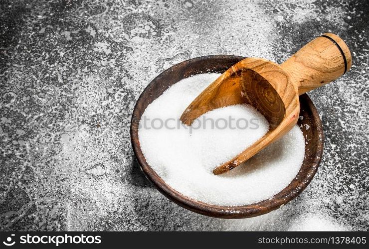 Sugar with a scoop in a bowl. On a rustic background.. Sugar with a scoop in a bowl.