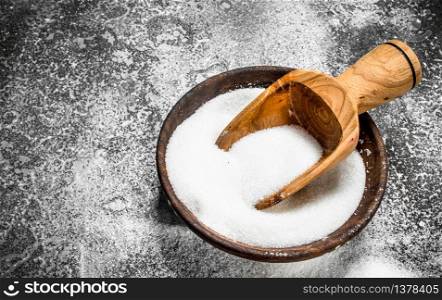 Sugar with a scoop in a bowl. On a rustic background.. Sugar with a scoop in a bowl.