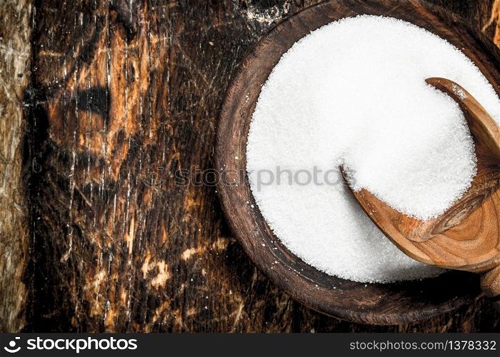 Sugar with a scoop in a bowl. On a wooden background.. Sugar with a scoop in a bowl.