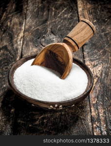 Sugar with a scoop in a bowl. On a wooden background.. Sugar with a scoop in a bowl.