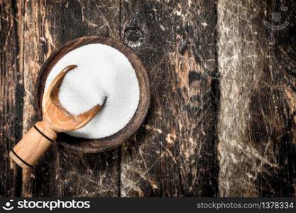 Sugar with a scoop in a bowl. On a wooden background.. Sugar with a scoop in a bowl.