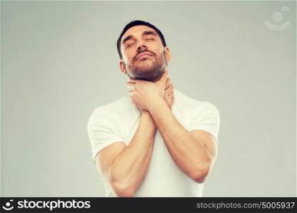 suicide, despair, death and people concept - young man choking himself by hands over gray background. young man choking himself over gray background