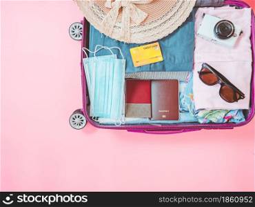 suitcase bag with clothing and accessories on pink background. Summer vacation travel with coronavirus pandemic.