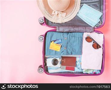 suitcase bag with clothing and mask on pink background. Summer vacation travel with coronavirus pandemic.