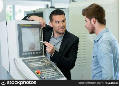 suited man training apprentice technician to use computer monitor