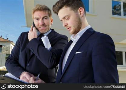 suited men talking on telephone outside of residential property