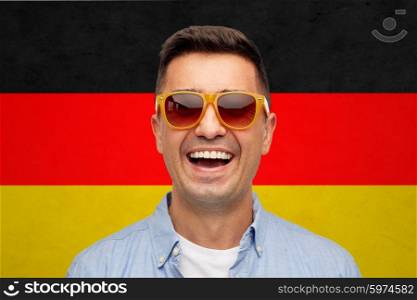 summer, accessories, patriotism, citizenship and people concept - face of smiling middle aged latin man in shirt and sunglasses over german flag background