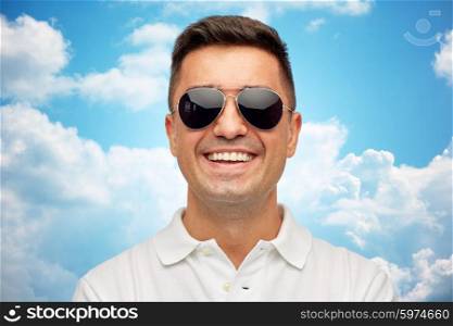 summer, accessories, style and people concept - face of smiling middle aged latin man in white polo t-shirt and sunglasses over blue sky and clouds background
