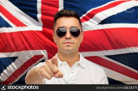 summer, accessories, style and people concept - middle aged latin man in white polo t-shirt and sunglasses pointing finger over brittish flag