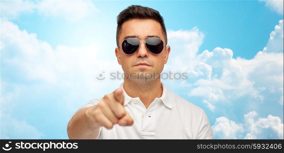 summer, accessories, style, gesture and people concept - face of middle aged latin man in white polo t-shirt and sunglasses pointing finger on you over blue sky and clouds background
