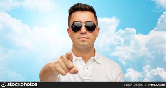 summer, accessories, style, gesture and people concept - face of middle aged latin man in white polo t-shirt and sunglasses pointing finger on you over blue sky and clouds background