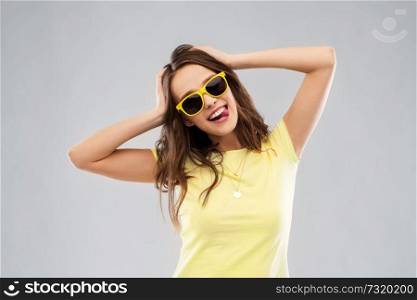 summer, accessory and people concept - smiling young woman or teenage girl in yellow t-shirt and sunglasses holding to her head over grey background. teenage girl in yellow sunglasses and t-shirt