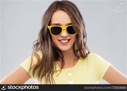 summer, accessory and people concept - smiling young woman or teenage girl in yellow t-shirt and sunglasses over grey background. teenage girl in yellow sunglasses and t-shirt