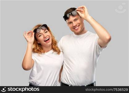 summer accessory, eyewear and people concept - portrait of happy couple in white t-shirts and sunglasses over grey background. happy couple in white t-shirts and sunglasses