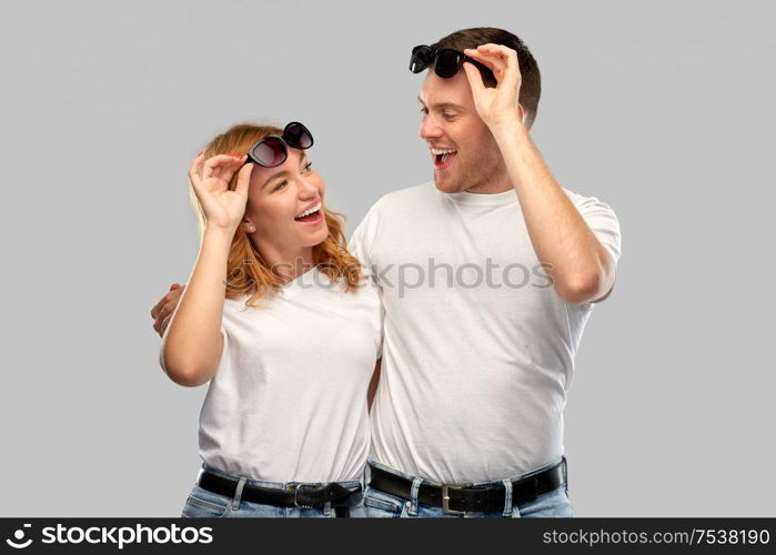 summer accessory, eyewear and people concept - portrait of happy couple in white t-shirts and sunglasses over grey background. happy couple in white t-shirts and sunglasses