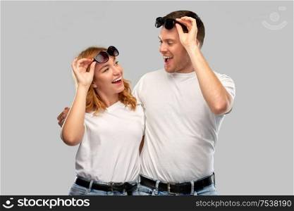 summer accessory, eyewear and people concept - portrait of happy couple in white t-shirts and sunglasses over grey background. happy couple in white t-shirts and sunglasses