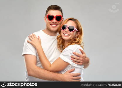 summer accessory, valentines day and love concept - portrait of happy couple in white t-shirts and heart shaped sunglasses over grey background. happy couple in white t-shirts and sunglasses