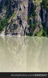 Summer Alps mountain landscape with turbid water reservoir lake and steep rocky slopes, Switzerland