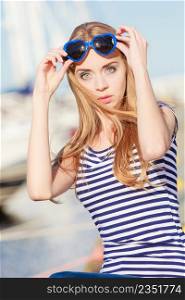 Summer and people concept. Fashion lovely blonde girl with heart shaped sunglasses in marina against yachts in port