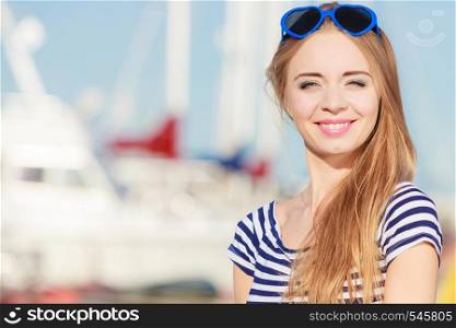 Summer and people concept. Fashion lovely blonde girl with heart shaped sunglasses in marina against yachts in port